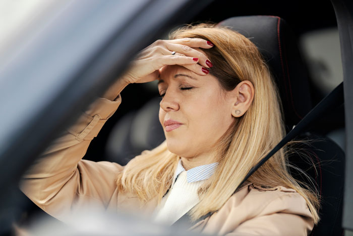Woman looking stressed in a car, hand on forehead, after family drama involving her stepmom and stepsisters.
