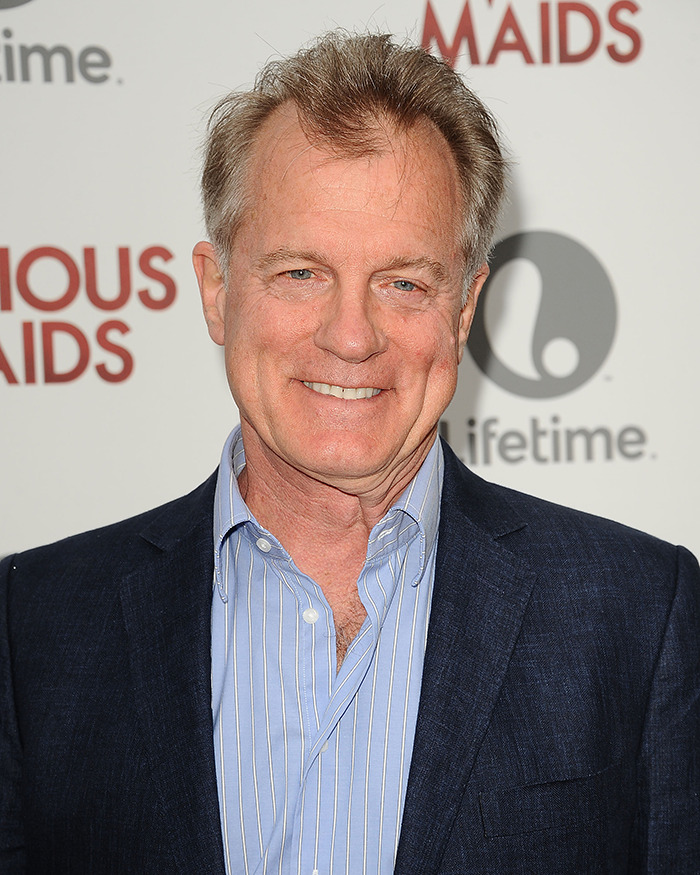 Disgraced actor at event, wearing a blue suit and striped shirt, with a backdrop featuring logos.