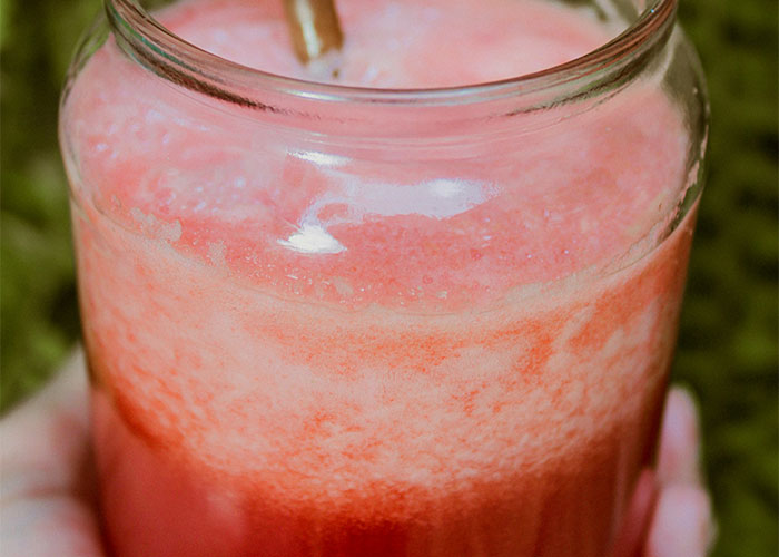 Close-up of a hand holding a jar of pink frothy drink with a straw.