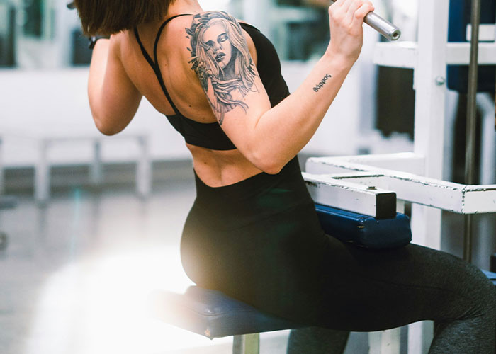 Woman with tattoo using gym equipment, illustrating bizarre gym scene.
