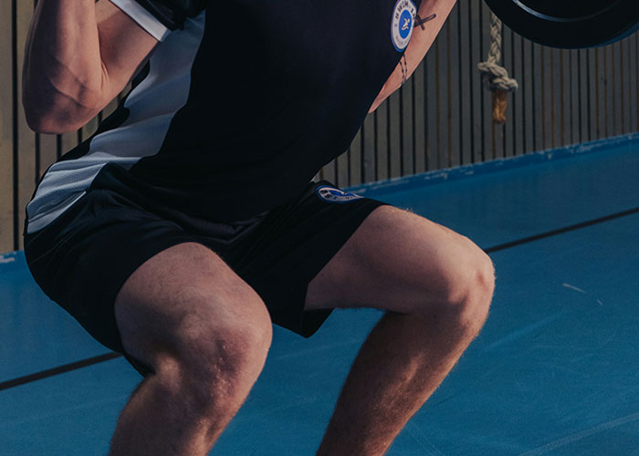 Man performing a squat at the gym with weights, wearing a black and white sports outfit.