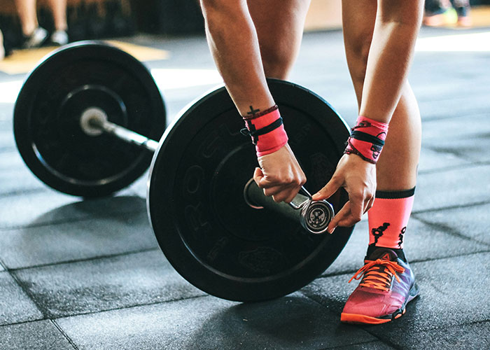 Person adjusting weights on a barbell at the gym, wearing bright workout gear.