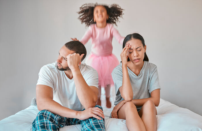 Parents looking tired while child jumps on the bed, a glimpse into the weirdest thing society accepts as normal.