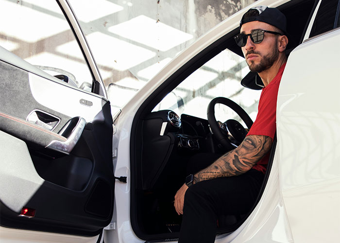 Man sitting in a white car, wearing sunglasses and a red shirt, related to wild reasons for lawsuits.