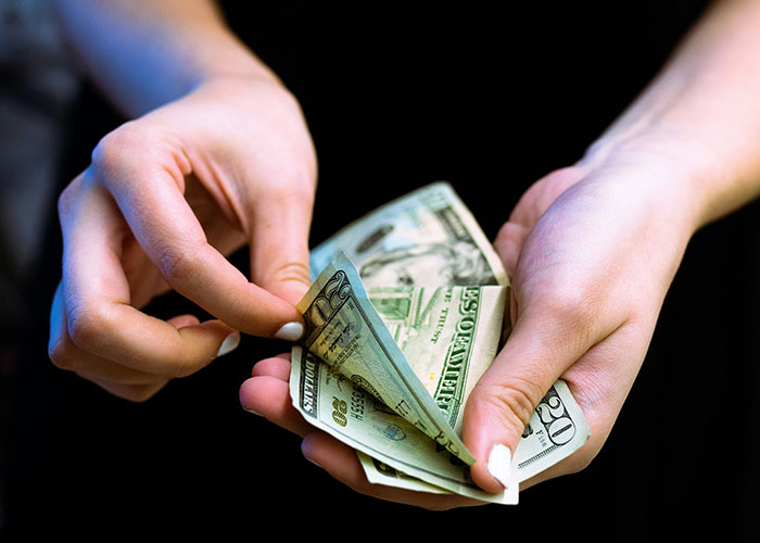 Hands holding US dollar bills, symbolizing reasons to sue someone.