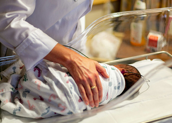 A newborn wrapped in a hospital blanket, overseen by a healthcare professional.