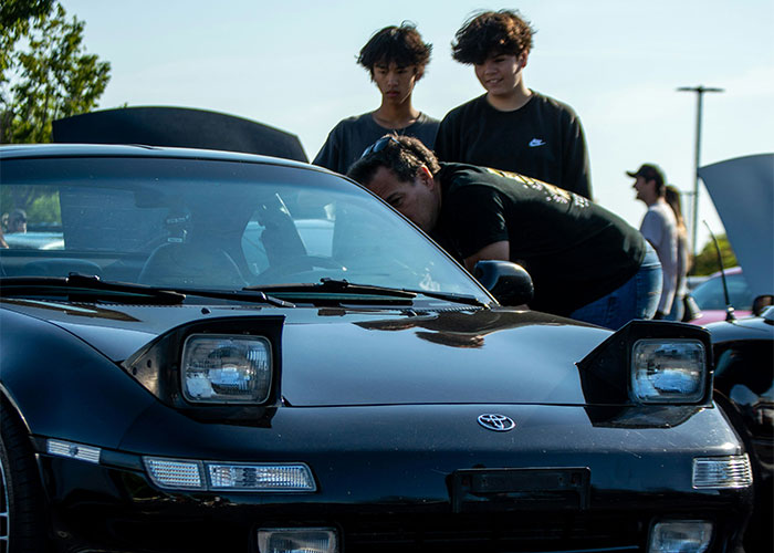 A person inspecting a black Toyota car with two onlookers, capturing a moment from a legal dispute scenario.