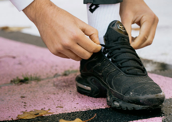 Hands tying laces on black sneakers, emphasizing unique reasons people sue, set on a pink and gray pavement background.