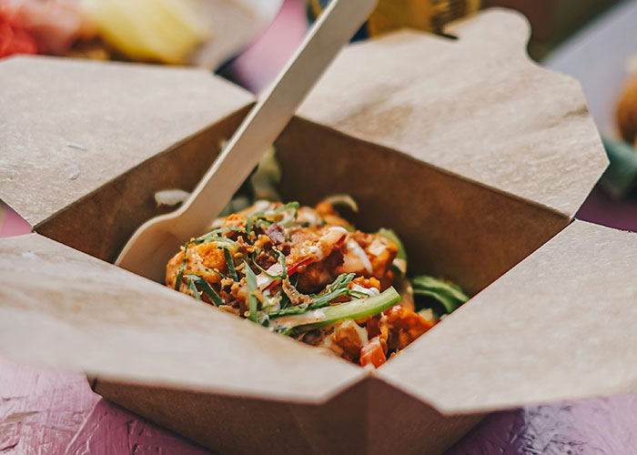 Takeout food in a cardboard box with a wooden fork, highlighting reasons people might choose to sue over food experiences.