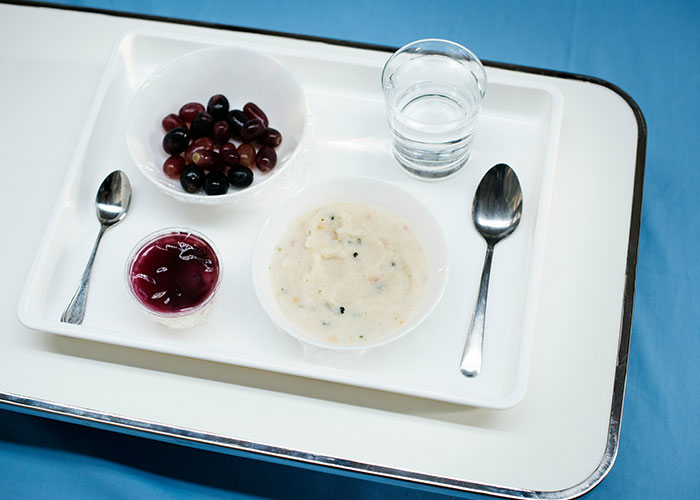 A tray with hospital food, including grapes, gelatin, soup, and a glass of water, representing reasons people sue.