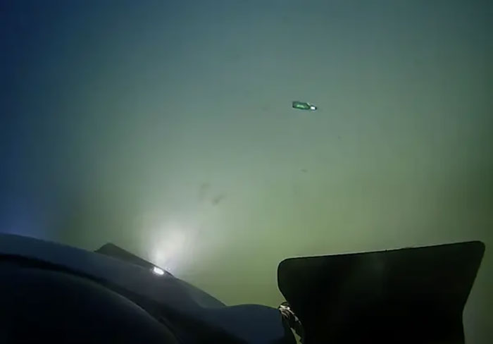 A submarine exploring iconic underwater site, with a bottle visible in the distance, illuminated by its headlights.