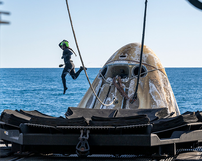Astronaut exiting capsule onto ship after ocean landing, with health concerns raised by doctors observing new images.