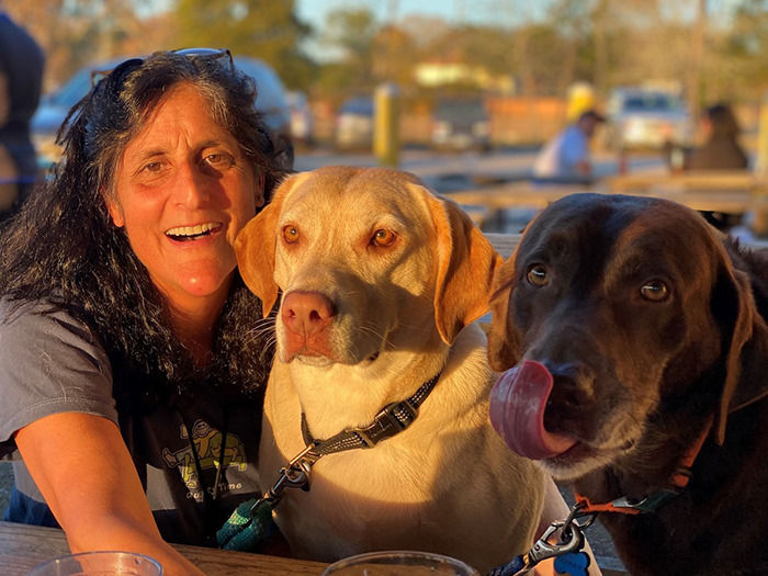 Smiling person with two dogs at an outdoor table, related to NASA astronaut's psychological trauma.