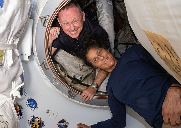 Astronauts smiling inside a space capsule, illustrating effects of long-term space missions on the human body.