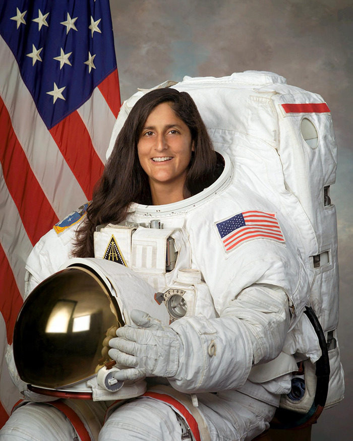 Astronaut in space suit, smiling near American flag, with health concerns discussed by doctors.