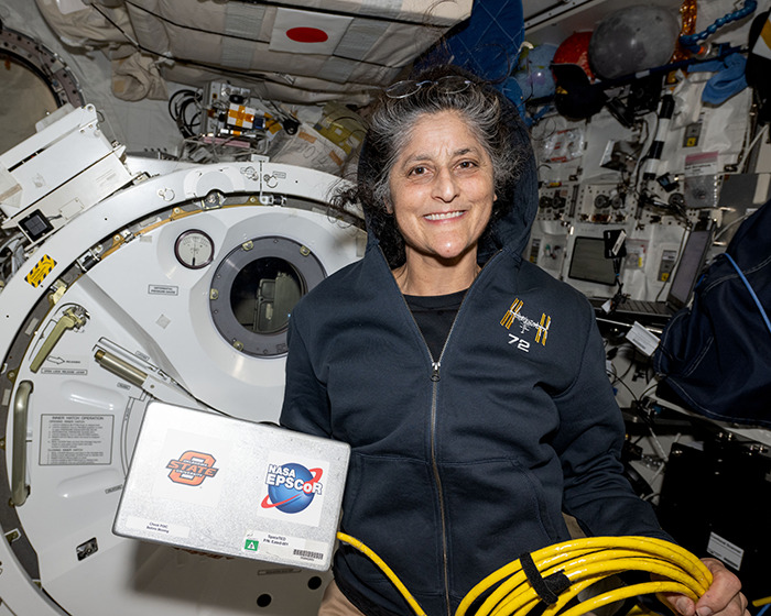 NASA astronaut holding equipment inside a spacecraft.
