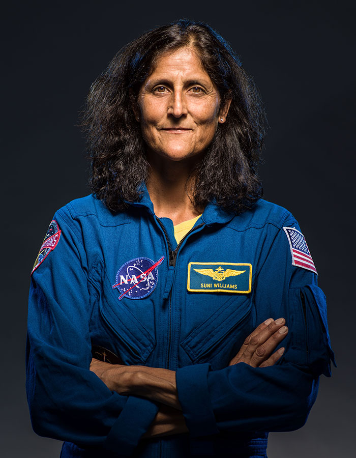 Astronaut in blue NASA suit, arms crossed, showing effects of space travel.