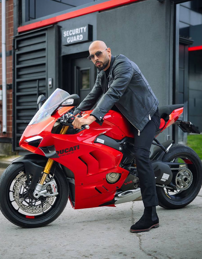 Biker in a black jacket posing on a red Ducati motorcycle in front of a security guard office. Biker in a black jacket posing on a red Ducati motorcycle in front of a security guard office.