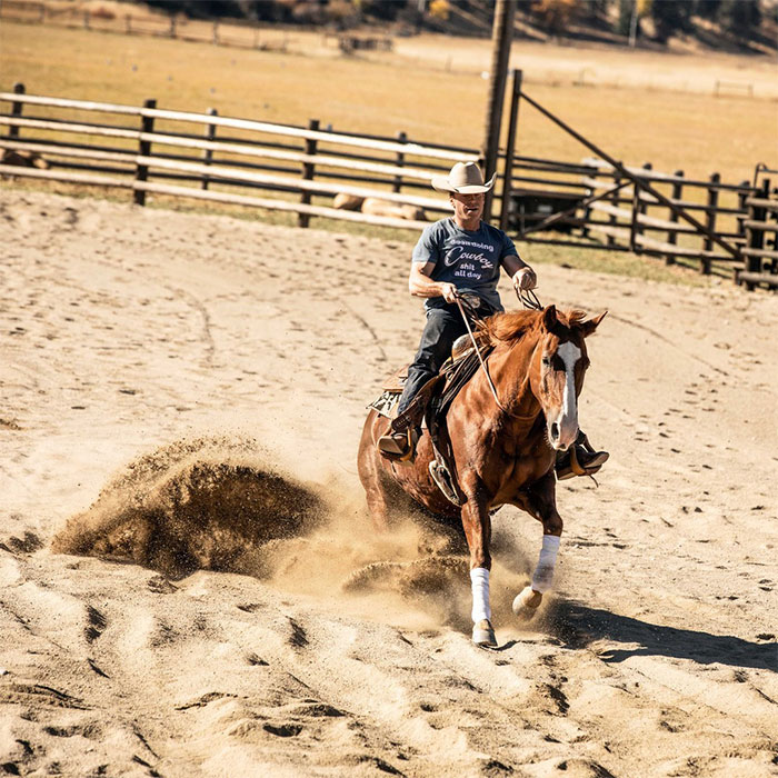 Taylor Sheridan riding a horse in a dusty arena, showcasing Western skills.