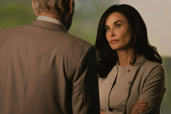 Woman in a beige suit listens intently to man, relevant to Taylor Sheridan's net worth discussion.