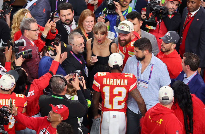 Taylor Swift with Travis Kelce at a crowded football event, surrounded by fans and photographers.