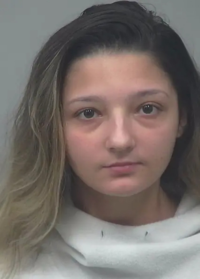 Young woman involved in a prom dress heist, wearing a white hoodie, showing a neutral expression.