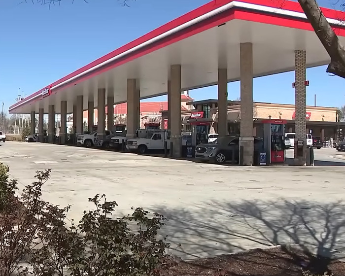 Gas station involved in prom dress heist brawl, with cars parked under canopy on a clear day.