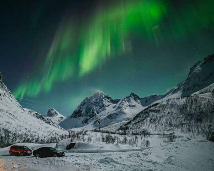 Northern lights over snowy mountains and parked cars, showcasing a hyped natural wonder meeting expectations.