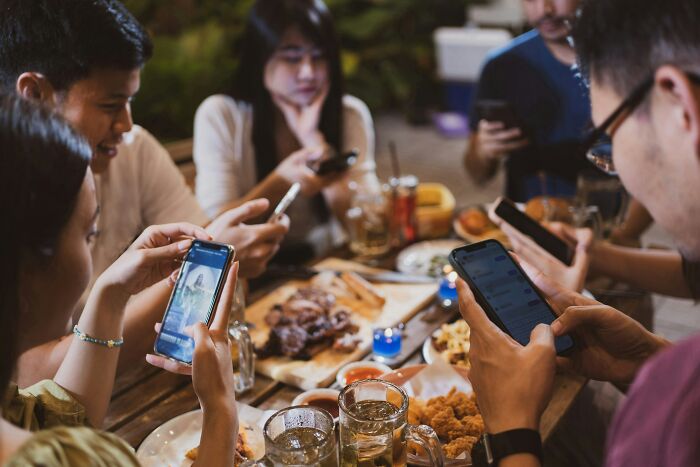 People dining and using smartphones, capturing a hyped experience that meets their expectations.