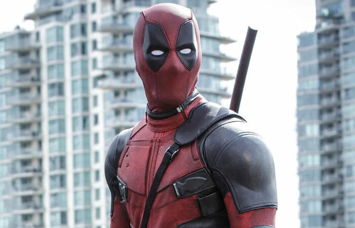 A superhero in a red and black costume stands confidently with city buildings in the background, capturing hyped expectations.