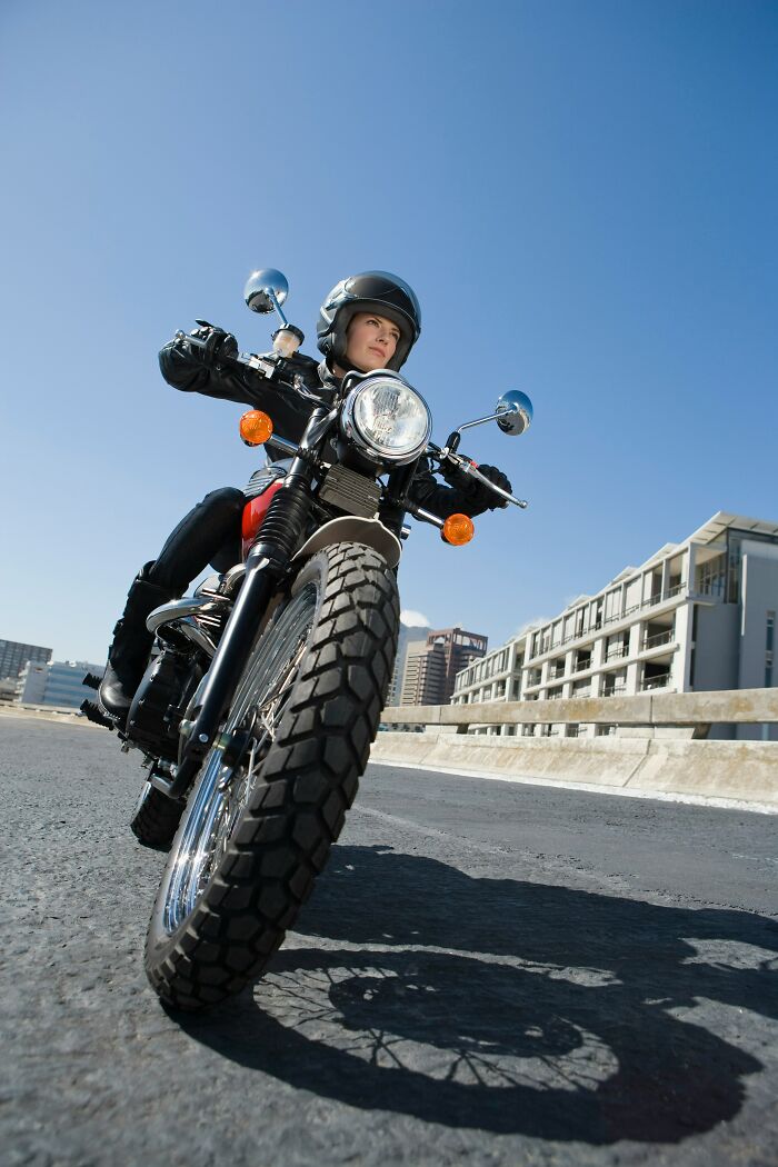 Motorcyclist riding confidently on the road, high expectations and adventurous spirit in cityscape backdrop.