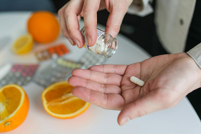 Hands pouring a pill, with sliced oranges and blister packs, highlighting unknowns about the human body.