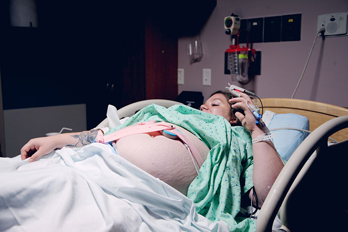 Pregnant woman in a hospital bed, wearing a monitoring device. Focus on human body mysteries in health care.
