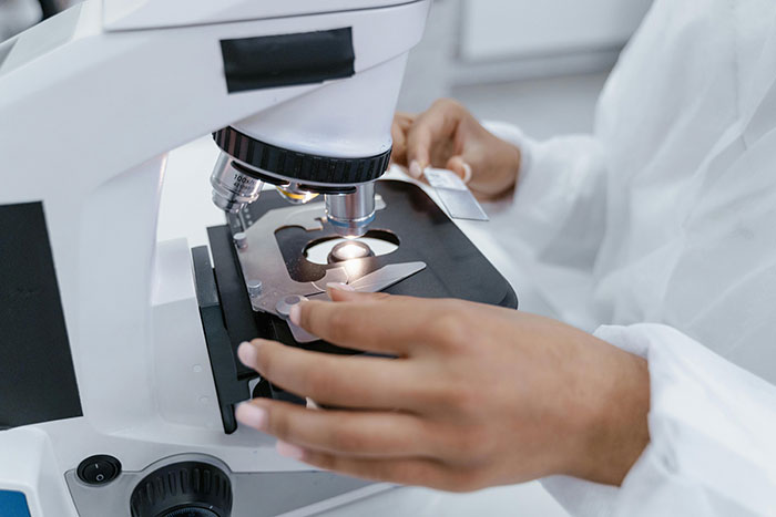 Researcher in lab coat using a microscope, exploring unknown aspects of the human body.