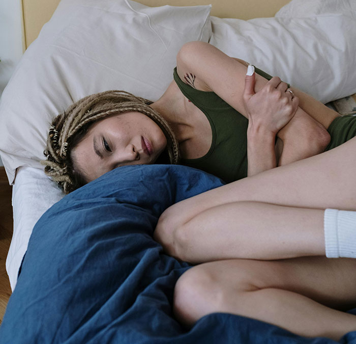 A person with dreadlocks lying in bed, contemplating unknown aspects of the human body.