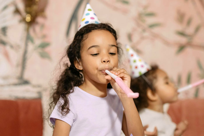 Children at a birthday party, wearing hats and blowing noisemakers, highlighting inclusion and celebration.