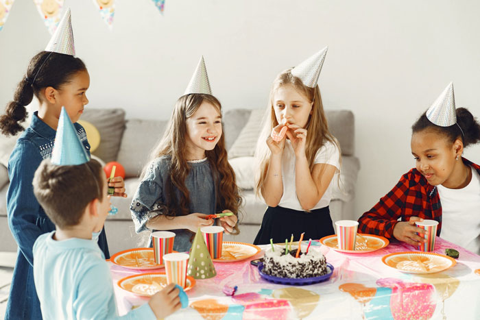 Children at birthday party wearing hats, eating cake.