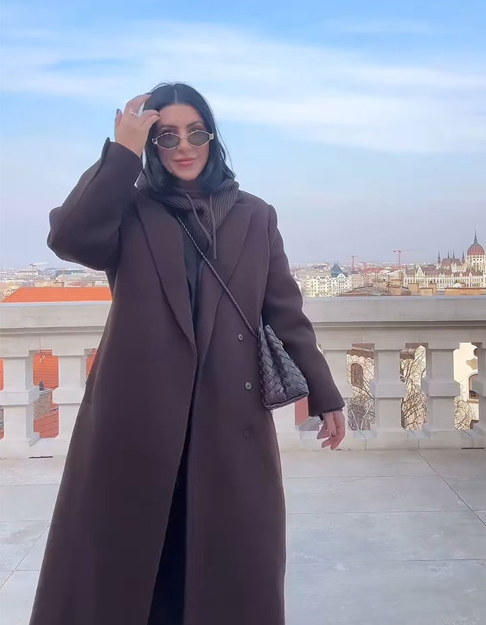 Millennial woman in coat and sunglasses standing on a balcony, embracing a child-free lifestyle.