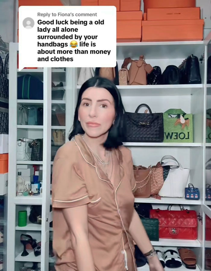 Millennial woman in front of handbags, facing backlash for a child-free lifestyle, wearing a beige top in a room full of accessories.