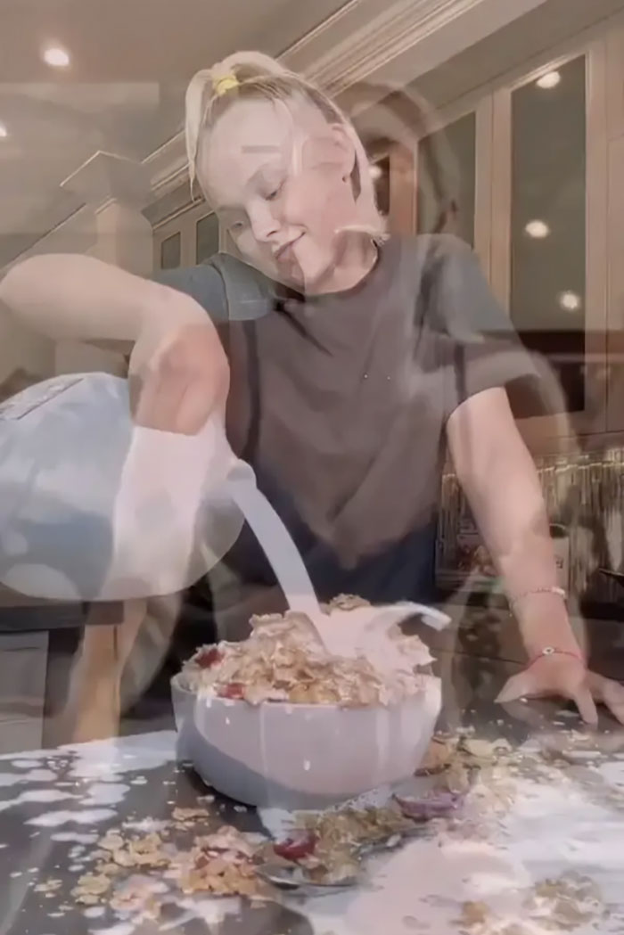 Celebrity pouring milk over overflowing cereal, showcasing a wasteful act in a kitchen setting.