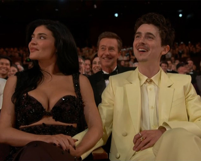 Kylie Jenner and Timothee Chalamet sitting and smiling at an event, capturing a lively moment amidst a crowd.