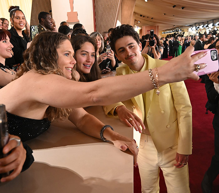 Celebrities posing for selfies with fans on the Oscars 2025 red carpet, capturing behind-the-scenes moments.