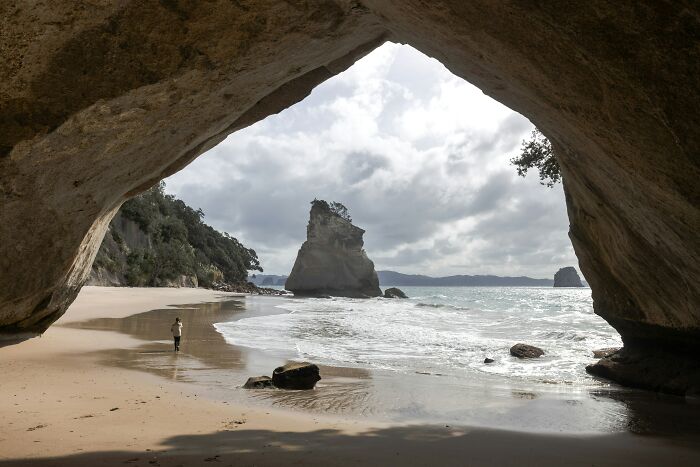 Stunning beach view framed by a rock arch, with waves gently lapping the sandy shore.
