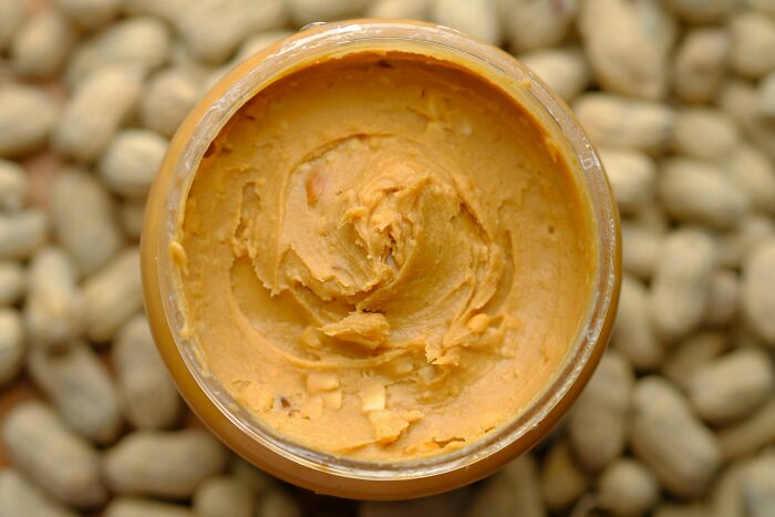 Creamy peanut butter in a jar, surrounded by peanuts, enhancing life with simple pleasures.