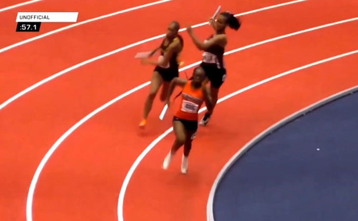 Track star running in a relay race, holding a baton on an indoor track.