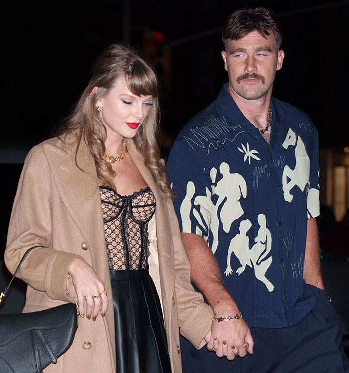 A couple holding hands, the woman in a stylish coat and lace top, and the man in a patterned shirt, enjoying a date night look.