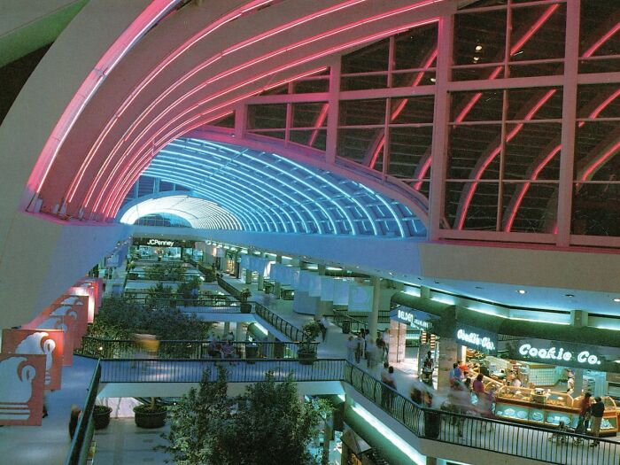 Vintage mall interior with neon lights and bustling food court activity.