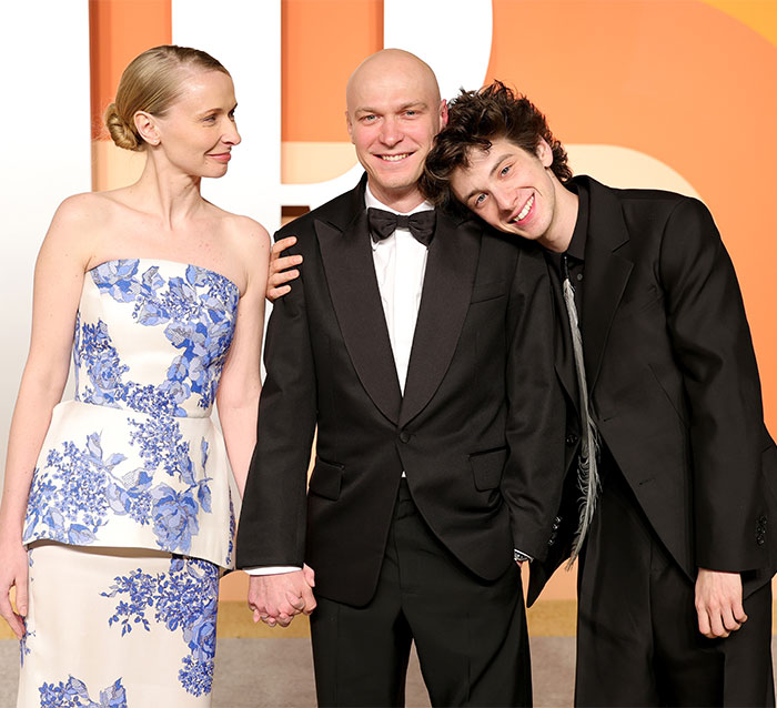 Three people at the Oscars 2025, one in a floral dress and two in black tuxedos, sharing a candid moment.