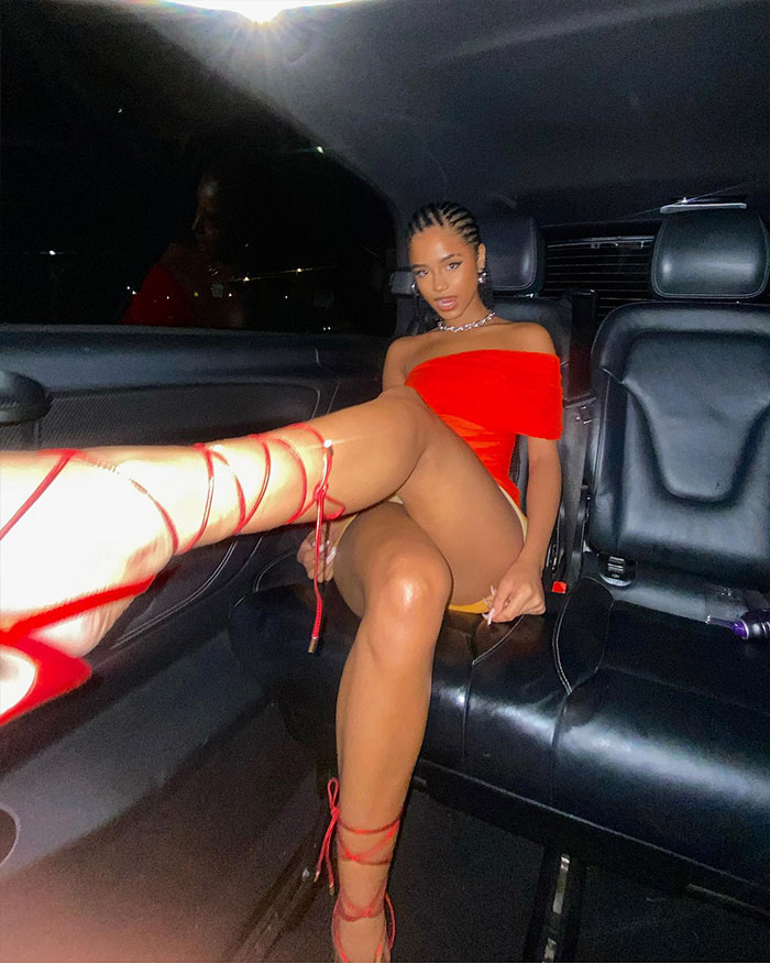 Singer Tyla in a car wearing a red dress and heels, showcasing her style and height in a dynamic pose.