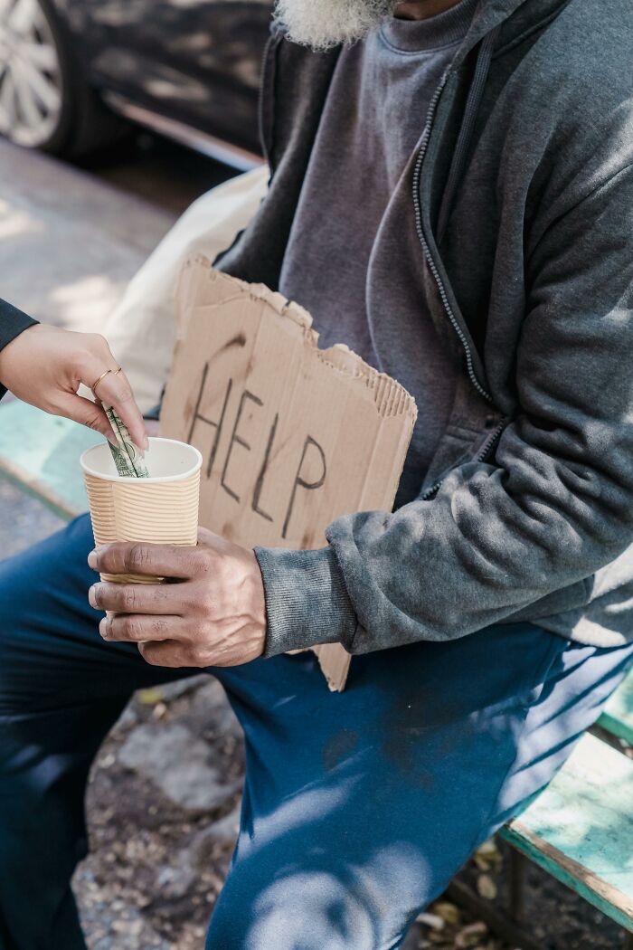 Undercover cop giving money in a cup to a person holding a "Help" sign.